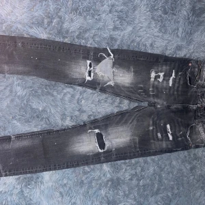 Grå slitna jeans från Supply & Demand - Säljer ett par grå jeans från Supply & Demand med slitningar och hål på benen. Jeansen har dragkedja och knapp i midjan samt en tvättad look som ger en cool vibe. Passar perfekt till soft-stilen.