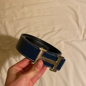 Blått bälte med silverfärgat H-spänne - Snyggt blått bälte med ett stort H-format spänne i silverfärg. Bältet har vita sömmar längs kanterna och är gjort i skinn. Perfekt accessoar för att lyfta din outfit.
