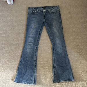 True Religion bootcut jeans i blå denim - Säljer ett par klassiska blå bootcut jeans från True Religion med snygg broderad bakficka och snygga slitningar, säljer dessa av anledning att dem är för stora. Jeansen har låg midja och silverfärgade knappar med logga. Perfekta för dig som gillar en tidlös jeanslook. Ordinarie pris: 1400 kr.