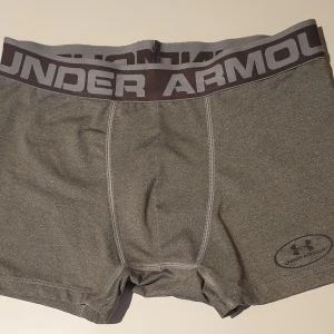 Grå boxershorts från Under Armour - Gråa boxershorts från Under Armour med bred resår i midjan och logga framtill. Tillverkade i syntetmaterial med loose passform, perfekta för träning eller vardag. Diskret logotyp på benet och bekväm design.