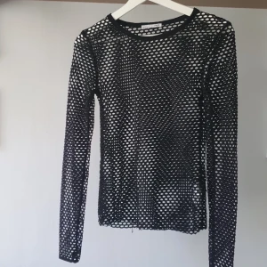 Svart nätmönstrad långärmad topp från Zara - Säljer en svart långärmad topp från Zara i nätmaterial. Tröjan har ett genomgående hålmönster och rund halsringning. Perfekt att styla lager på lager för en trendig look. Använd fåtal gånger men har ändå någon enstaka tråd längst ner men det syns knappt (se bilder). 