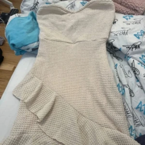 Krämfärgad axelbandslös klänning med volang - Säljer en söt axelbandslös klänning i krämfärgat, aldrig använt eftersom att den var för tight. Perfekt inför sommaren, studentfest osv