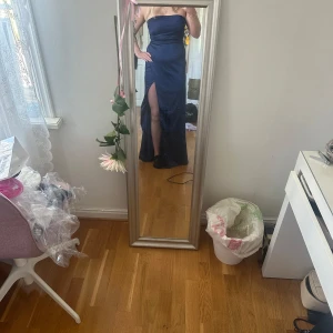 Marinblå axelbandslös långklänning med slits - Säljer en marinblå axelbandslös långklänning i glansigt material. Klänningen har en hög slits framtill och figurnära passform upptill. Perfekt för festliga tillfällen och nu till balen,  har en elegant siluett. 