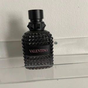 Valentino Uomo Born in Roma Eau de Toilette 50ml - En lyxig herrparfym från Valentino i en svart, nitar-inspirerad flaska. Doften har mineraliska och träiga toner med inslag av violblad, salt, ingefära, salvia, vetiver och fräscha gröna nyanser. Perfekt för dig som gillar unika och moderna dofter. Ganska välanvänd ungefär 1/3 kvar av flaskan 