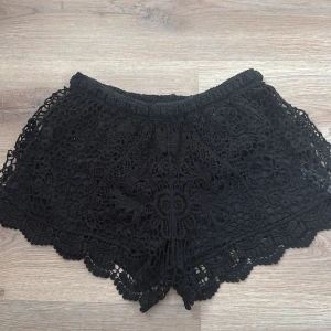 Svarta spets shorts med volangkant - Säljer ett par svarta shorts med snygg spets och detaljerad broderad design. De har elastisk midja och volangkant längst ner som ger en extra touch. Passformen är loose och materialet känns som bomull med spets ovanpå. Perfekta för sommarens alla tillfällen!