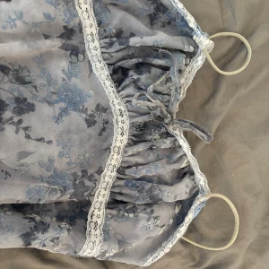 Blommig blå långklänning med spets - Säljer en romantisk långklänning med blommigt mönster i blå och grå toner från urban outfitters. Klänningen har smala axelband, söt spetskant och snörning vid bysten. Materialet känns lätt och flowy, perfekt för sommarkvällar. Slitsar nertill ger extra rörelse och stil. Står inte vilken storlek det är men jag skulle säga att den passar någon med storlek S.