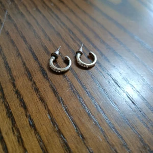 Guldiga örhängen med stenar - Snygga små guldiga örhängen i halvcirkel-form med glittrande stenar på framsidan. Perfekta för att ge din look lite extra bling och passar till både chill och mer uppklädda outfits. Lätta att bära och stilrena.