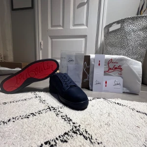 Mörkblå Christian Louboutin sneakers - Snygga mörkblå sneakers från Christian Louboutin i mocka med klassisk röd sula och signaturlogo undertill. Skorna har rund tå, platt sula och snörning framtill. Perfekt för dig som vill sticka ut med exklusiv stil och detaljer som syns.