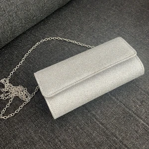 Silver kuvertväska med kedja - Snygg silverfärgad kuvertväska med glittrig yta och metallkedja som axelrem. Väskan har ett stilrent, rektangulärt format och stängs med magnetlås. Perfekt för att lyfta din outfit med lite extra bling.