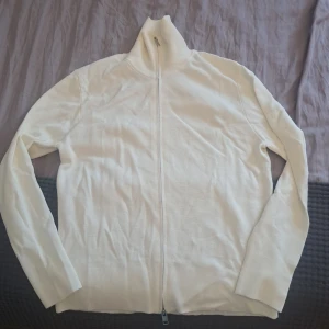 Vit kofta med dragkedja från H&M - Vit kofta från H&M i regular fit med hel dragkedja framtill och hög krage. Långärmad och i mjukt material som passar perfekt till lager-på-lager. Enkel och clean stil som funkar till det mesta.