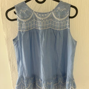 Blå broderad blus från Mango - Supersöt ljusblå blus från Mango med broderade detaljer och hålmönster upptill och längst ner. Ärmlös modell med volangkant nertill och knytning i nacken. 