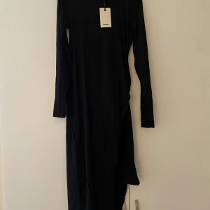 Svart omlottklänning från Bik Bok - Säljer en svart lång omlottklänning från Bik Bok med lång ärm och snygg v-ringning. Klänningen har ett tunt, ribbat material som ger en cool struktur och faller snyggt längs kroppen. Perfekt för dig som gillar stilrena och enkla plagg med en twist.