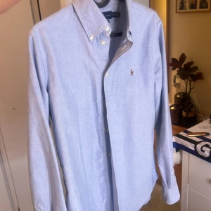 Ljusblå skjorta från Ralph Lauren M - Säljer en klassisk ljusblå skjorta från Ralph Lauren i custom fit. Skjortan har button down-krage, broderad logga på bröstet och långa ärmar. Tillverkad i mjuk bomull och passar perfekt till jeans eller chinos.