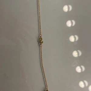 Guldigt armband med s-formad detalj - Snyggt och minimalistiskt armband i guldton med en tunn kedja och en s-formad detalj i mitten. Perfekt för dig som gillar stilrena smycken med en twist. Passar att kombinera med andra armband för en personlig look.