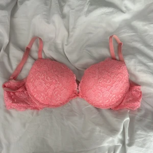 Rosa spets-bh från Cubus  - Supersöt rosa bh från cubus med blommig spets, vadderade kupor och justerbara axelband. Framtill sitter en liten rosett och en metallcharm. Spetsdetaljer längs kanterna och klassisk knäppning bak. 