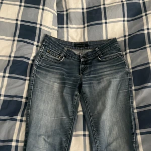 Bootcut jeans från Stockh LM, blå - Bootcut jeans från Stockh LM i tvättad blå färg med snygga slitningar och ljusare partier. Klassisk femficksmodell, bälteshällor och dragkedja. Jeansen har bredare ben och rå kant nedtill för en cool vibe
