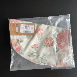 Newbie Blommig mössa, storlek 48/50 - Söt mössa med blommigt mönster i rosa och grönt på en vit bakgrund från Newbie. Tillverkad i mjuk bomull, perfekt för dig som gillar romantiska och fräscha accessoarer.