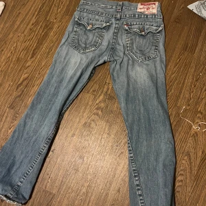 True Religion bootcut jeans vintage - Säljer dessa true religion bootcut jeans för att det är för stora på mig, strl är W30/W31. Som man ser på bild 5 och 6 så är det 2 hål ett hål som jag själv har täckt med tyg från ett par andra jeans (man kan ju säkert ta bort det om man hellre vill ha ett hål där.) och det andra hålet var redan där när jag köpte dem. Tycker dock det är snyggt med dessa hål! Både tjejer och killar kan ha dessa jeans, antingen som baggy (om det är för stora) eller som vanliga bootcut jeans! Pris går att diskutera