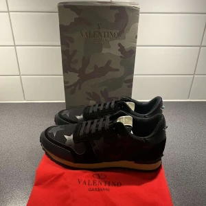Valentino Garavani Rockrunner sneakers - Snygga svarta Valentino Garavani Rockrunner sneakers med stjärnmönster och coola detaljer. Skorna har svart mocka och textil, svarta snören och en beige sula. Perfekta för dig som vill sticka ut med exklusiva och trendiga sneakers.