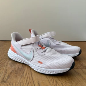 Nike sneakers  - Nike sneakers i ljuslila med korall och silver detaljer. Skorna har kardborreband, elastiska snören och mjuk, stötdämpande sula. Storlek 35, använd fåtal gånger, i väldigt bra skick. 