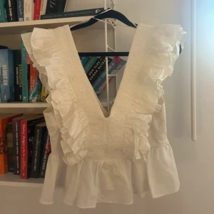 Vit blus med volanger och v-ringning - Supersöt vit blus med djup v-ringning och breda volanger längs axlarna. 