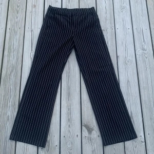 Svarta randiga kostymbyxor Kappahl - Svarta kostymbyxor från Kappahl med vita tunna ränder. Byxorna har raka ben och klassisk passform med fickor fram och bak. 