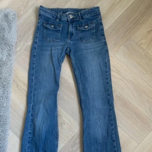 Blå bootcut jeans från Kappahl - Snygga blå jeans från Kappahl i storlek 152. Modellen har bootcut-ben, klassiska fickor fram med lock och knappar samt vanliga bakfickor. Jeansen är i denim med slitna detaljer nertill för en cool look. Ganska använda men inga tecken på det förutom att jag har lagt ner dem så dem blir 2-3cm längre. Nypris ca:300kr