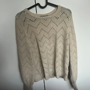 Beige glittrig stickad tröja Fransa - Säljer en beige stickad tröja från Fransa i storlek XS. Tröjan har ett glittrigt inslag och ett snyggt hålmönster i zickzack över hela plagget. Rund hals och långa ärmar med ribbade muddar. Perfekt för dig som gillar lite extra shimmer i vardagen.