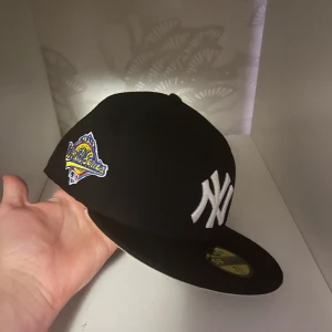 Svart New York Yankees keps - Snygg svart keps från New Era med New York Yankees-logga i vitt framtill och World Series-märke på sidan. Klassisk flat brim och broderade detaljer. Perfekt för dig som gillar sportig streetstyle och vill sticka ut med en ikonisk look. skriv för info! 