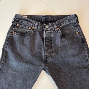Levi's 501 svarta/mörkgrå  jeans W32 L32 - Klassiska Levi's 501 jeans i en svart/mörkgrå färg. Rak passform samt knappgylf. Ett perfekt val för dig som vill ha en avslappnad men exklusiv look. HÖR AV DIG VID MINSTA FUNDERING….