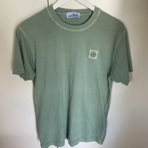 Grön t-shirt från Stone Island - Snygg ljusgrön t-shirt från Stone Island med klassisk logotyp-patch på bröstet. T-shirten har rund halsringning och korta ärmar, tillverkad i mjuk bomull som känns skön mot huden. Perfekt för dig som gillar stilrena och trendiga plagg.