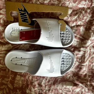 Nike Victori One vita sandaler strl 38 (ge bud) - Nike Victori One Shower Slide i helvitt med präglad swoosh på ovansidan. Sandalerna har öppen tå och platt sula med strukturerad fotbädd för extra komfort. Perfekt för chill dagar eller efter träning. Snygg och enkel design som funkar till allt. Oanvända! Nypris ca 300 kr 