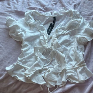 Vit linnetopp med volanger och snörning - Supersöt vit linnetopp från H&M med volanger längs halsringningen och nederkanten. Toppen har korta ärmar och snygg snörning framtill som ger en romantisk vibe. Perfekt för sommarens alla häng! Materialet är linne och toppen är lätt och luftig.