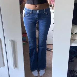 Blå bootcut jeans med låg midja - Snygga blå jeans med bootcut-modell och låg midja. Jeansen har klassiska fickor fram och bak, samt en smickrande passform som sitter tajt upptill och släpper ut vid benen. Perfekta för dig som gillar en retro vibe och vill ha ett par jeans som sticker ut.