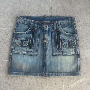 Blå jeanskjol med fickor och dragkedjor - Säljer en cool blå jeanskjol med slitna detaljer, stora fickor fram och bak, samt dragkedjor och knappar med röda sömmar. Kjolen har bälteshällor och en klassisk jeanslook som passar perfekt till sneakers eller boots. Midjemått: 36. Säljer fler kjolar på mitt konto! Använd gärna köp nu eller kom med prisförslag❤️