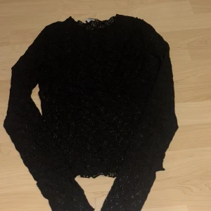 Svart spetsblus med lång ärm - Säljer en svart blus i spets med lång ärm och rund hals. Blusen har ett elegant och lite transparent utseende, perfekt för dig som gillar en stilren look med detaljer. Passar dig som vill ha något snyggt och enkelt att matcha med jeans eller kjol.