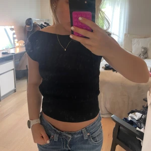 Svart ribbad stickad topp - Svart stickad topp med ribbade detaljer och korta ärmar. Sitter tajt och har en bredare mudd nedtill som ger en snygg passform. Perfekt att matcha med jeans eller kjol för en clean look.