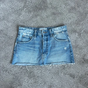 Jeanskjol med slitningar  - Supersnygg jeanskjol med slitningar som passar nu på sommaren för en trendig look!🩷🩷Midjemått:70 Längd fram:26 cm Längd bak:29 cm