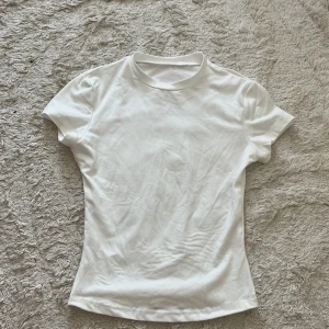Vit basic t-shirt i bomull - Enkel och stilren vit t-shirt med rund hals och korta ärmar. Modellen är figurnära och passar perfekt till alla typer av outfits. Tillverkad i mjuk bomull för en skön känsla hela dagen.