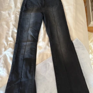 Svarta bootcut jeans med fickor - Snygga svarta jeans med bootcut passform och markerade sömmar längs benen. Framtill finns två stora fickor och baktill klassiska fickor med knappdetalj. Jeansen har en mörk tvätt och är tillverkade i ett stretchigt denimtyg.