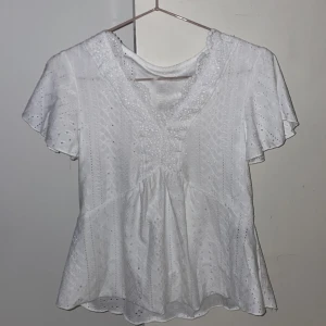 Vit spetsblus/topp  från SHEIN - Superfin vit blus/topp  från SHEIN med broderade spetsdetaljer och v-ringning. Blusen har korta, vida ärmar och ett romantiskt hålmönster över hela tyget. Perfekt för dig som gillar en söt och luftig stil med mycket detaljer.