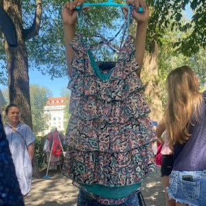 Paisleymönstrad volangklänning - Supersöt kort klänning med paisleymönster i blått, rosa och grönt. Klänningen har flera lager volanger och smala axelband som korsas i ryggen. Perfekt för varma dagar och ger en lekfull vibe.