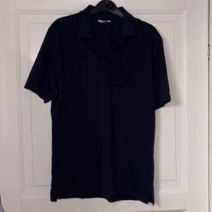 Mörkblå skjorta från East West - Snygg mörkblå skjorta från East West i storlek S. Skjortan har korta ärmar, klassisk krage och rak passform. Perfekt för dig som gillar en clean och stilren look. Materialet känns mjukt och bekvämt mot huden.