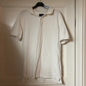 Vit pikétröja från Boomerang M - Klassisk vit pikétröja från Boomerang i storlek M. Tröjan har korta ärmar, krage och knäppning framtill. Tillverkad i mjuk bomull, perfekt för en clean och stilren look. Diskret logga på bröstet.