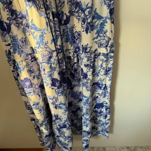 Blåvit långklänning från Holly & Whyte - Supersöt långklänning från Holly & Whyte med blått blommigt mönster på vit botten. Klänningen har snörning i midjan och är perfekt för sommarens alla tillfällen. Luftigt material och avslappnad passform. Är 173 och den är kort för mig därav inga bilder på!