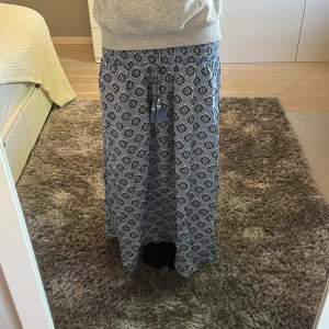 Blå långkjol med mönster från Gina Tricot - Superskön långkjol från Gina Tricot i blått med snyggt mönster och resår i midjan. Kjolen har knytband med tofsar framtill. Köpte den förra året men har endast använt 1 gång då den var lite för liten. Passar dig som är runt 160 cm lång! Skulle säga att den är som ny förutom att den har tappat några pärlor på toffsarna, (hör av dig för bild)!🌸