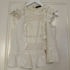 Vit volang blus från Zara Basic - Superfin vit blus från Zara Basic med broderade detaljer, volanger och en ärmlös model. Säljer pågrund av att jag inte passar bra i sånna här modeller och vill rensa bort det jag inte vill ha. Storleken är L men passar mig som har mellan XS-S.