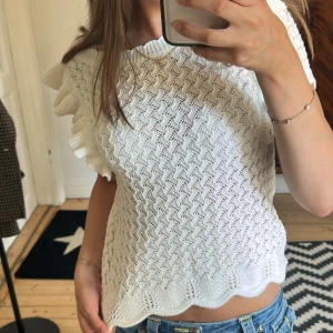 Vit stickad topp med volang från Lindex - Supersöt vit stickad topp från Lindex med volangdetaljer på axlarna och vågig nederkant. Toppen är knappt använd kanske 1 gång! Som ny! Nypris är 379kr men säljer för 190kr