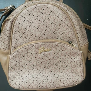 Beige ryggsäck från Guess med logomönster - ÄKTA KÖPT FÖR 1900 PERFEKT FÖÖR SLKOLAN PRISET KNA DISKUTERAS Säljer en beige ryggsäck från Guess med klassiskt logomönster över hela väskan. Väskan har guldfärgade detaljer, dragkedja och är tillverkad i syntetmaterial med skinnliknande känsla. Perfekt storlek för vardagens essentials och snygg att bära på ryggen.