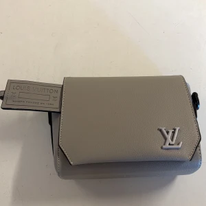 Beige axelväska från Louis Vuitton - Snygg beige axelväska från Louis Vuitton i slätt skinn med silverfärgad LV-logga framtill. Väskan har ett stilrent och modernt uttryck, dragkedja på baksidan och justerbar axelrem. Perfekt för dig som vill ha en exklusiv och clean look.